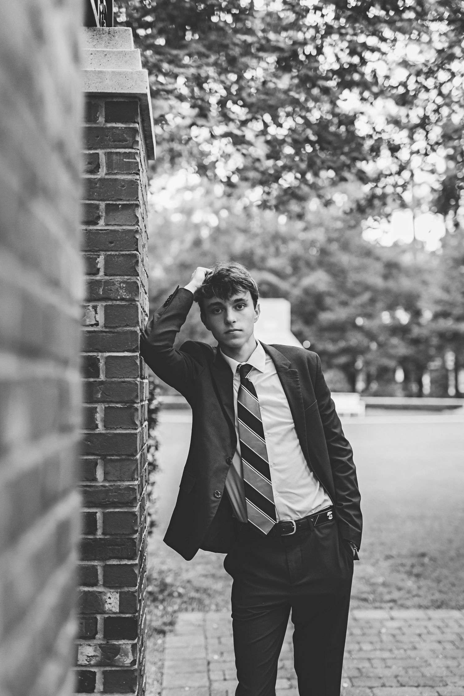 A person in business attire leans against a brick wall in a black and white photo.
