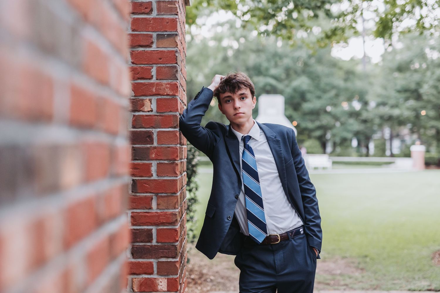 Casual pose leaning against brick wall in business attire with blurred background.