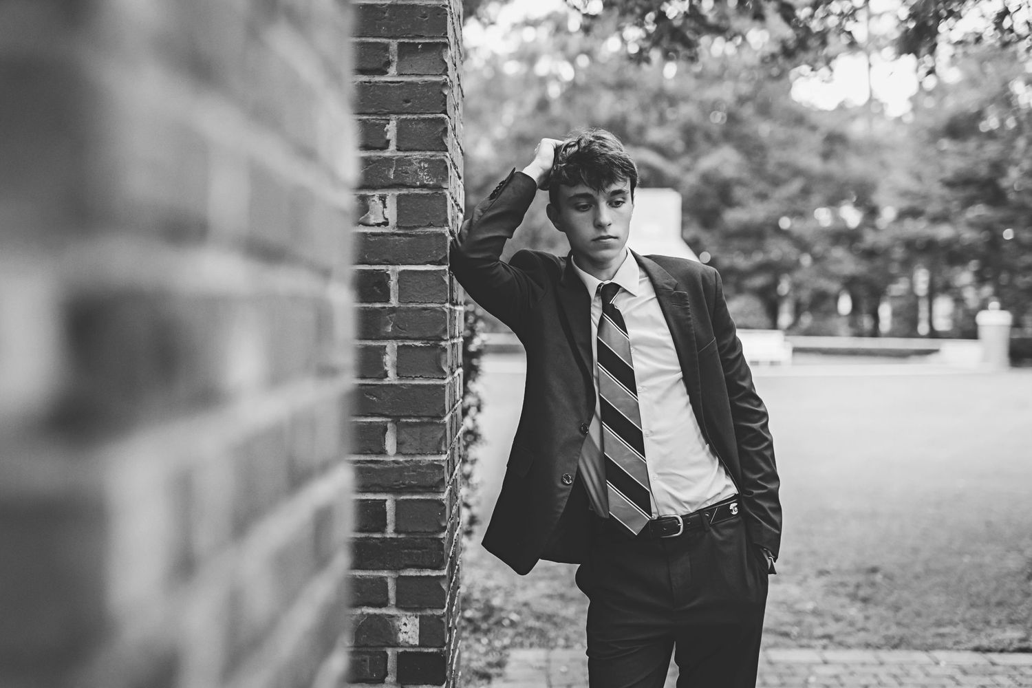 A casual portrait of someone in a suit and baseball cap leaning against brick architecture.