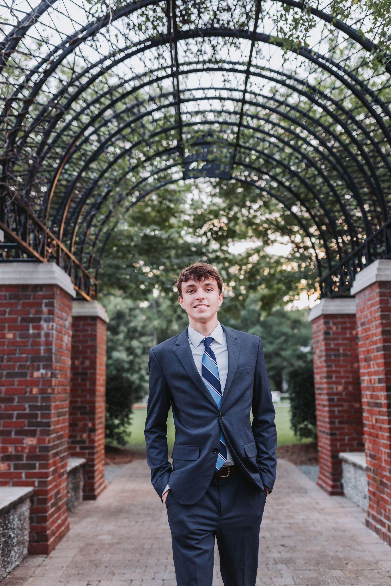 A formal portrait under an ornate iron pergola with brick columns and winding path.