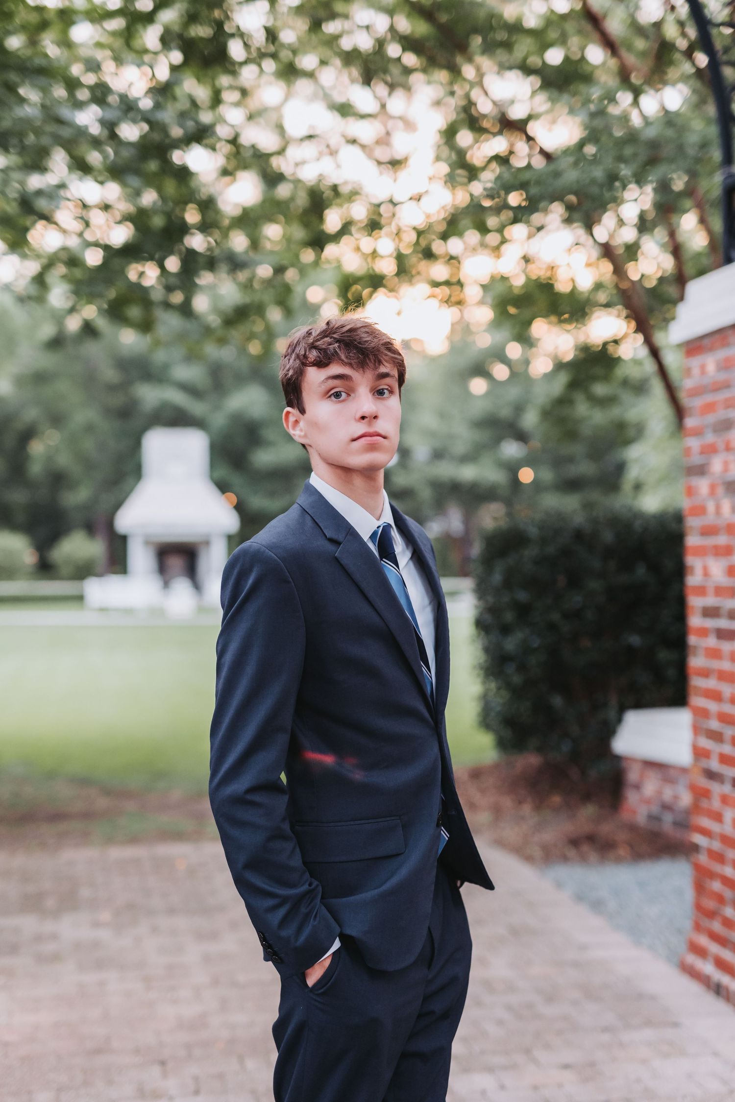 A formal portrait outdoors with bokeh lighting and brick architecture in the background.