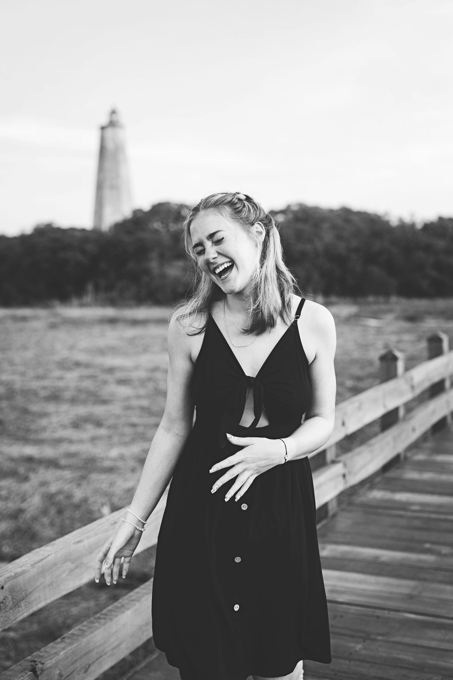 Candid black and white portrait showing joyful laughter on boardwalk with lighthouse view.