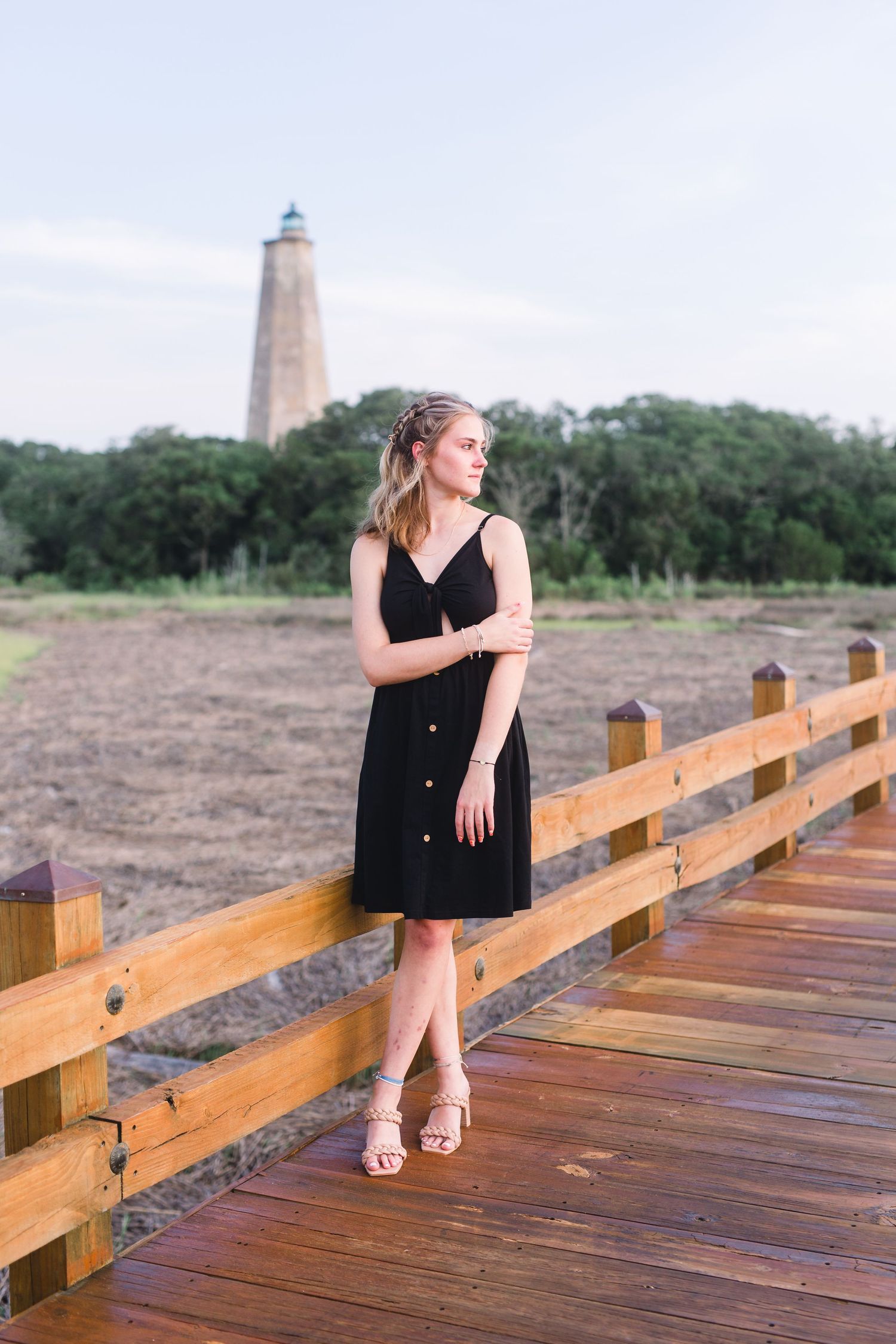 Black sundress against coastal backdrop with lighthouse and wooden boardwalk during summer photoshoot.