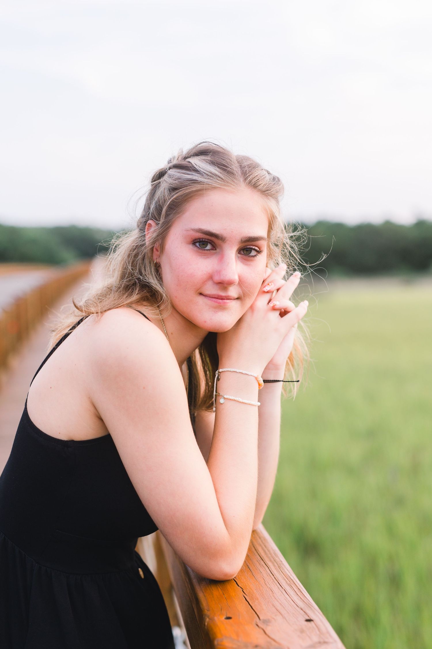 Portrait by wooden fence overlooking grassy field in summer evening light.