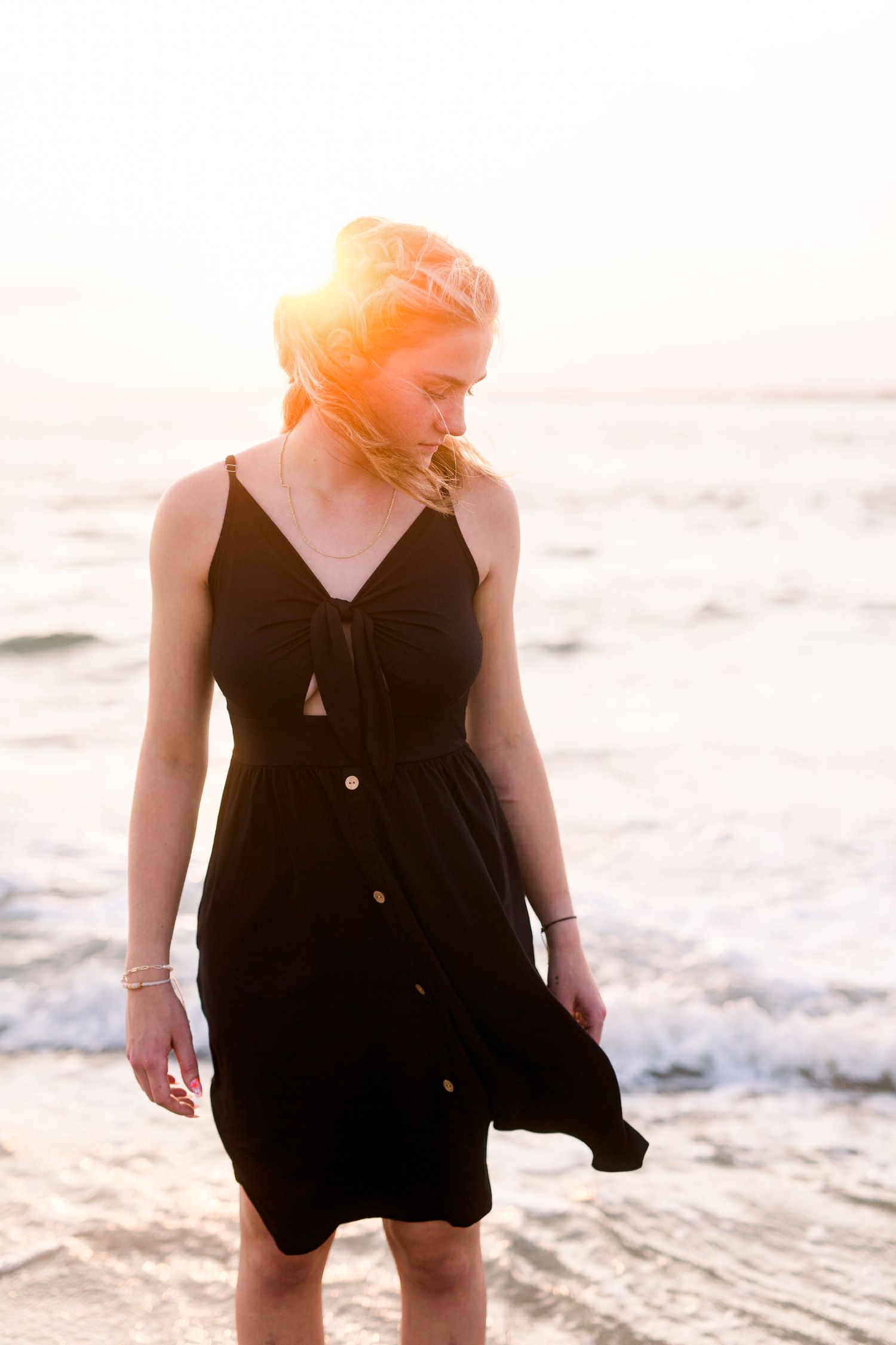 Woman in black sundress enjoying sunset on beach with gentle waves in background.