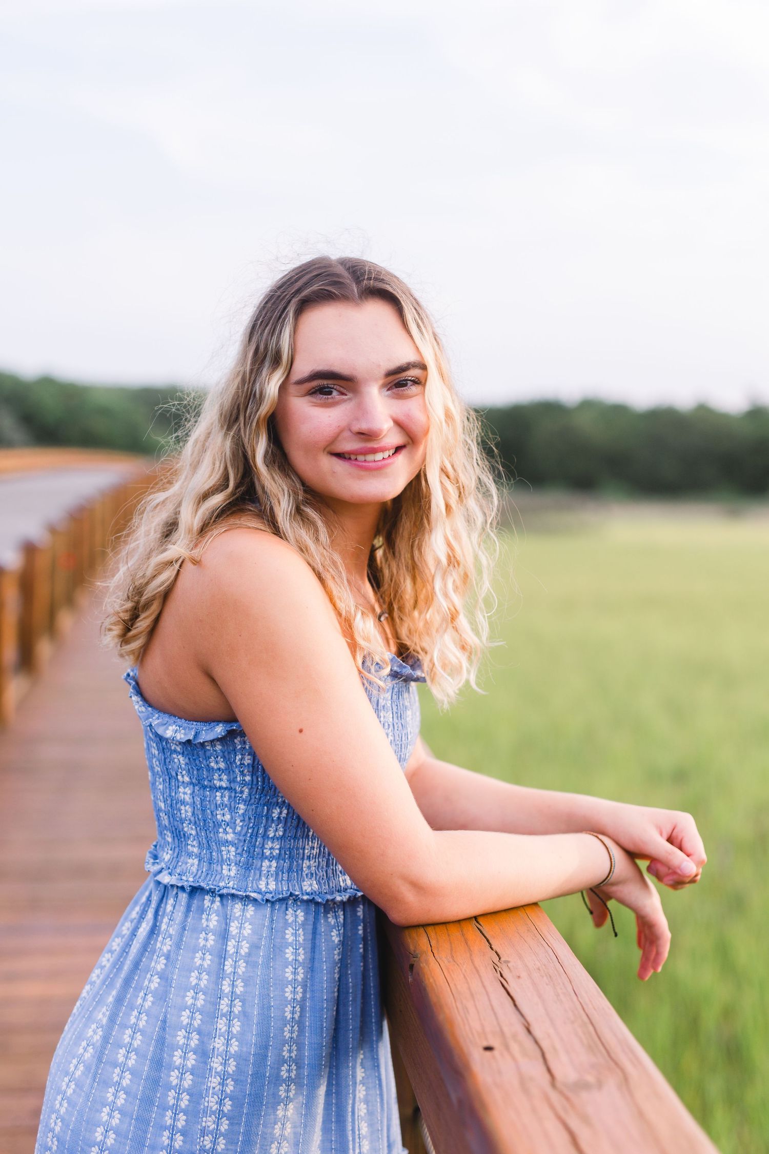 Summer portrait in blue patterned dress leaning on wooden railing with marsh views.