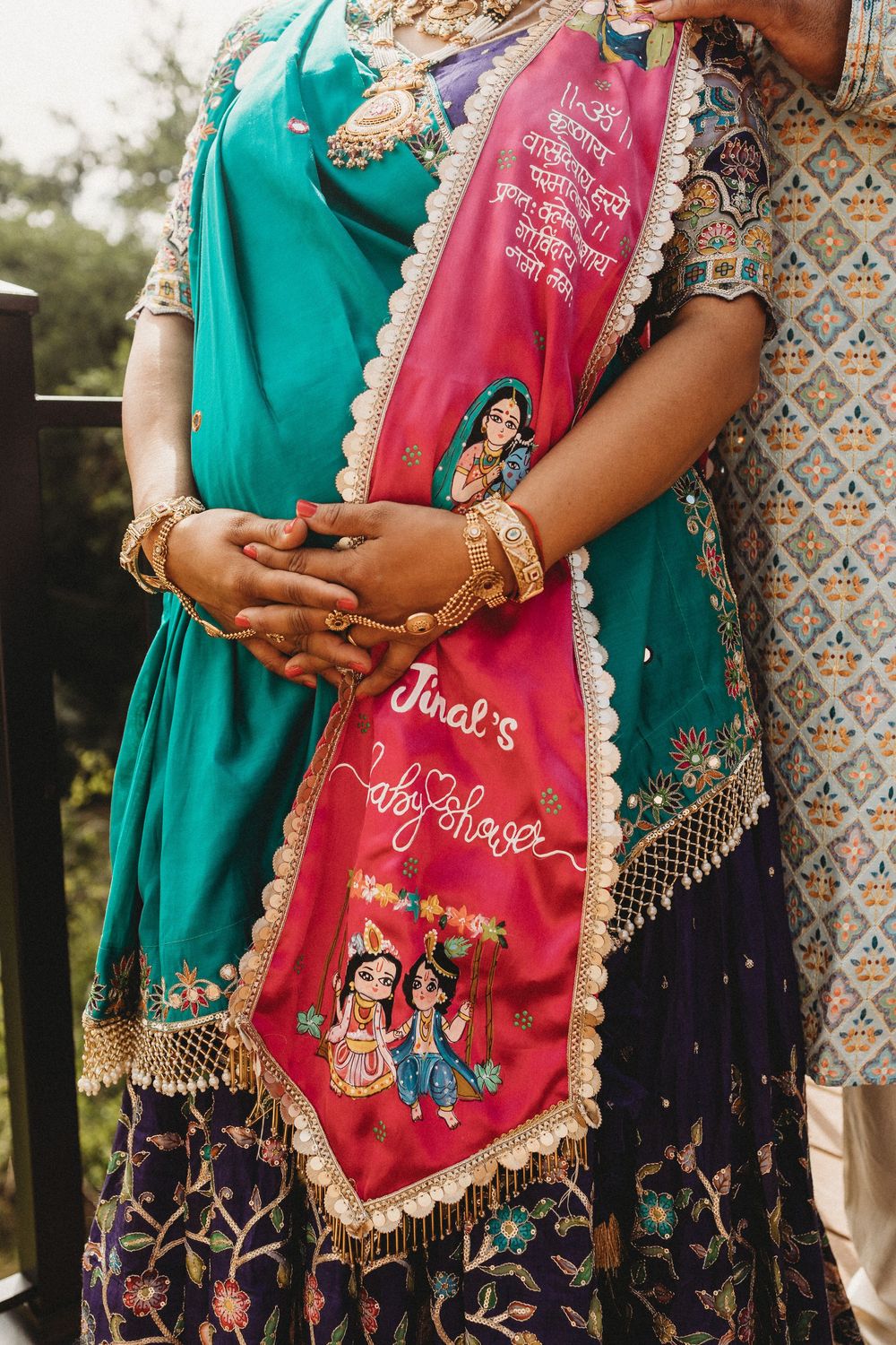 Close-up of embroidered pink dupatta with Radha Krishna motif and text on Indian maternity outfit.