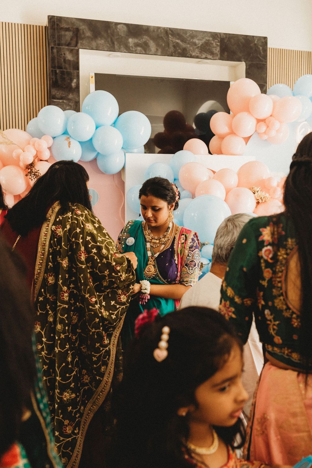 Women in colorful traditional Indian attire gather at a festive celebration decorated with pink and blue balloons.