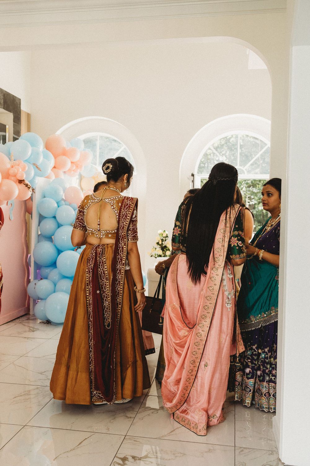 Women in traditional Indian attire at a festive celebration with pastel balloon decorations.