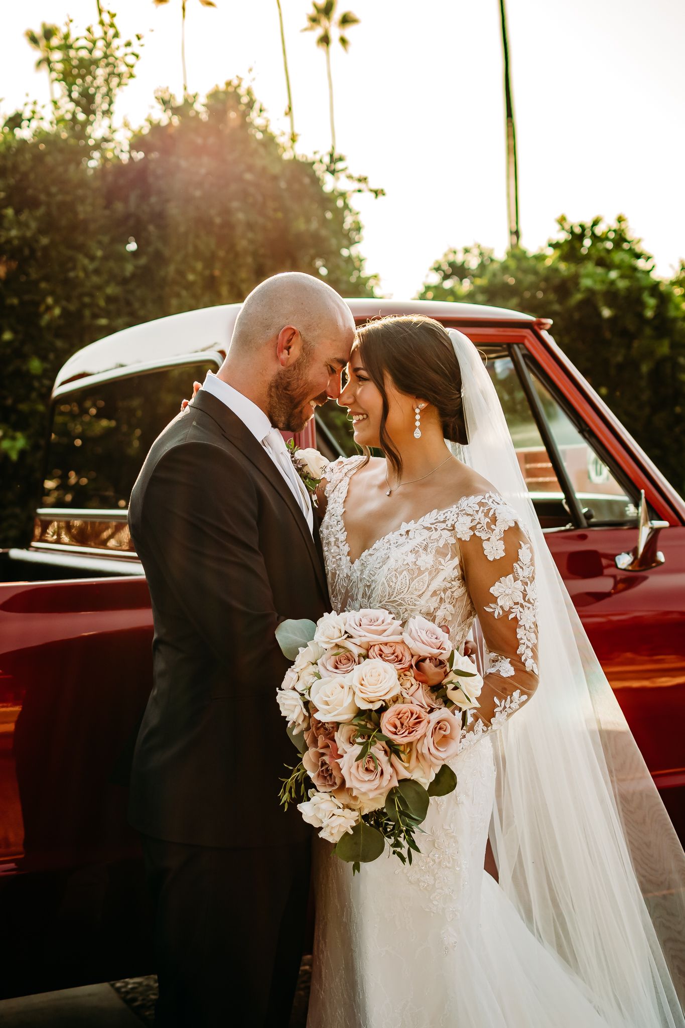 Couple embracing at golden hour sunset on mountain top, bride in lace gown, groom in vest and wide-brim hat.