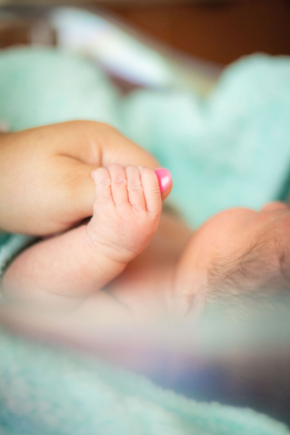 Close-up of a newborn baby's tiny hand and feet resting on a soft teal blanket.