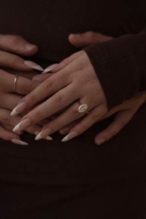 Close-up of hands with long white French tip nails wearing a gold diamond halo engagement ring on ring finger.