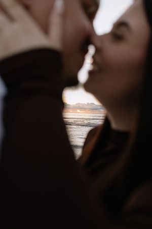 Couple sharing a romantic almost-kiss at sunset on the beach, framed by golden ocean light.
