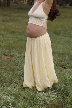 Side profile of pregnant woman in yellow skirt and crop top outdoors.