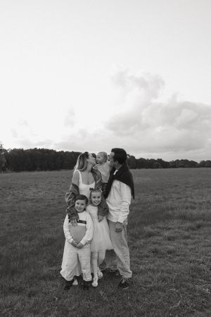Black and white family portrait of parents with three young children standing in an open field.