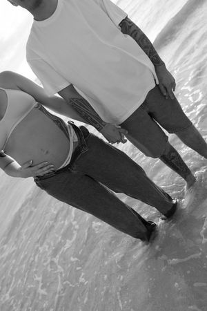 Black and white photo of a couple holding hands while standing in ocean waves at the beach.
