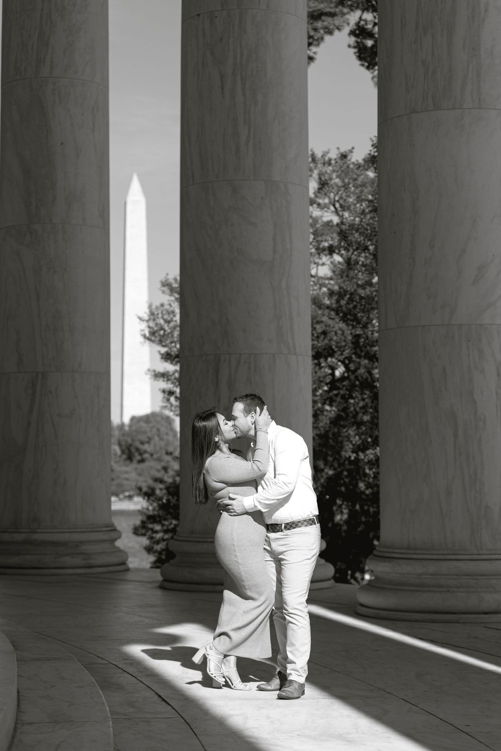 Couple kissing between columns at Jefferson Memorial with Washington Monument in background, black and white photo.