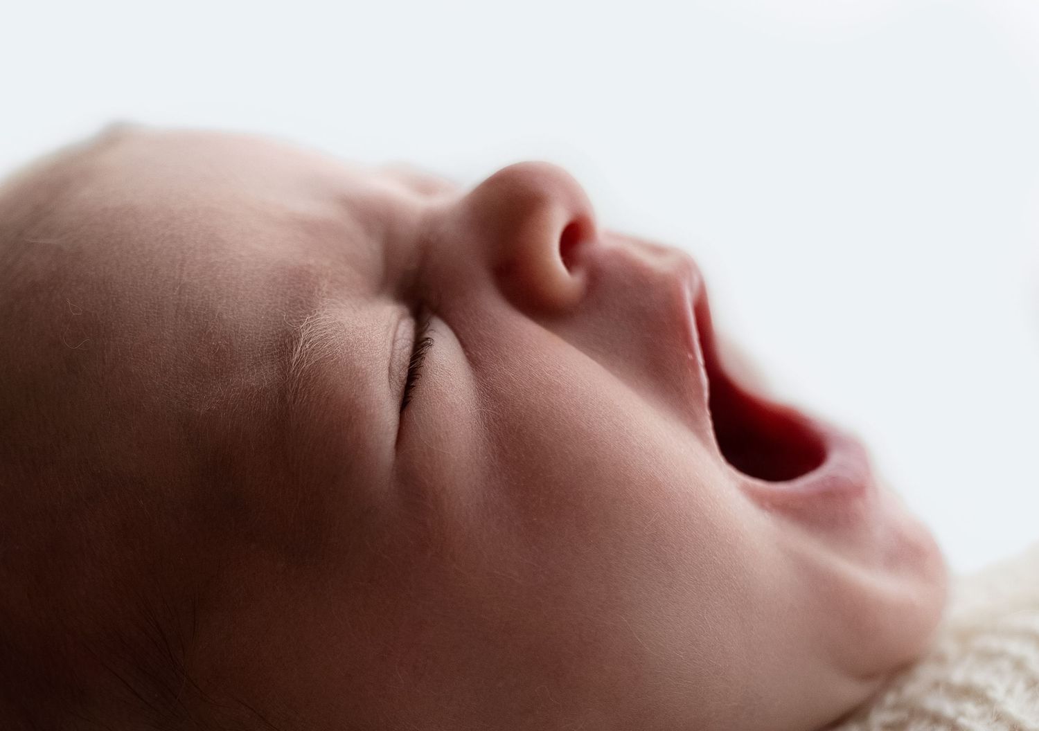 Newborn girl yawns as she gets cozy for a detail, backlit shot at Somerset Portraits studio, a Charlottesville baby photographer.