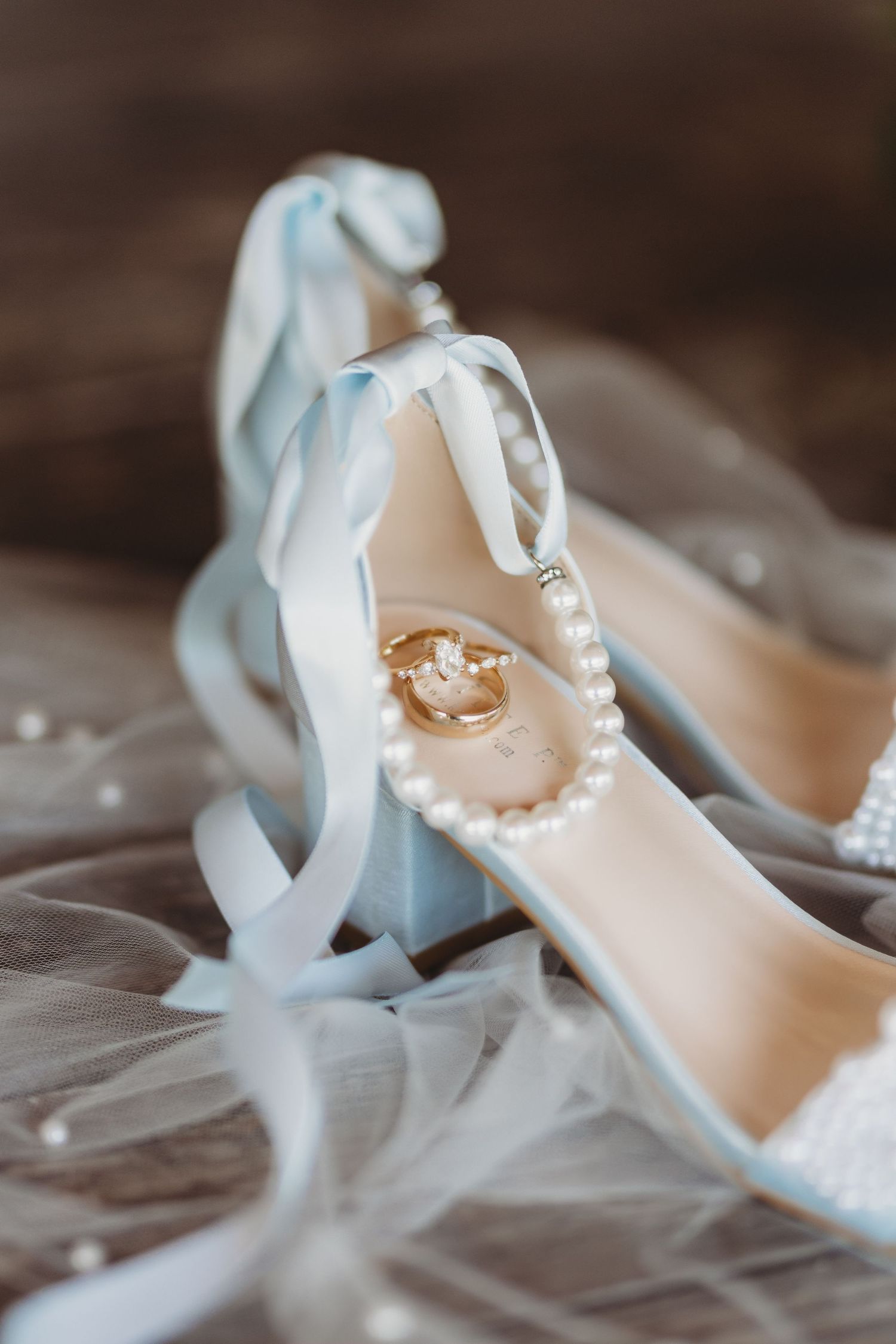 Light blue satin wedding heels with pearl bracelet and gold rings on white veil, elegant bridal accessories.