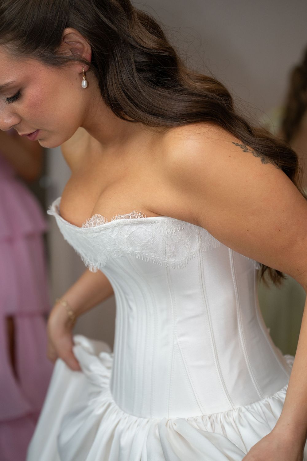 Bride in a white strapless corset wedding gown being helped into her dress on her wedding day.