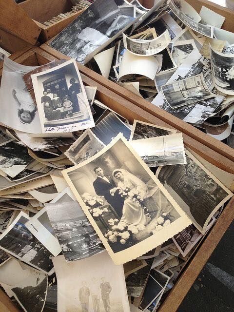 A wooden box overflowing with vintage black and white photographs, including a wedding portrait, scattered and piled together.