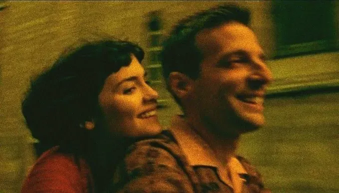 A smiling man and woman share a joyful moment together in a warmly lit, intimate scene.