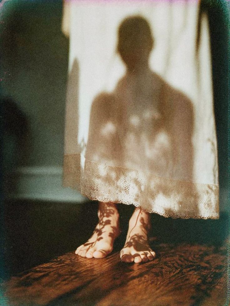 Shadow of a person silhouetted on sheer white curtain with bare feet visible on wooden floor.