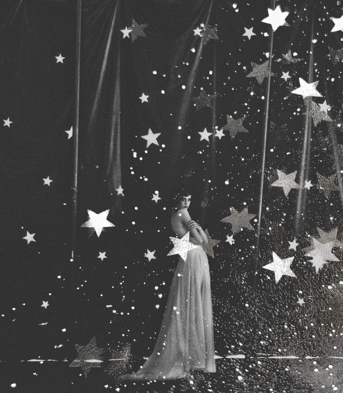 Black and white photo of a performer in flowing gown surrounded by glittering stars on a dark theatrical stage.