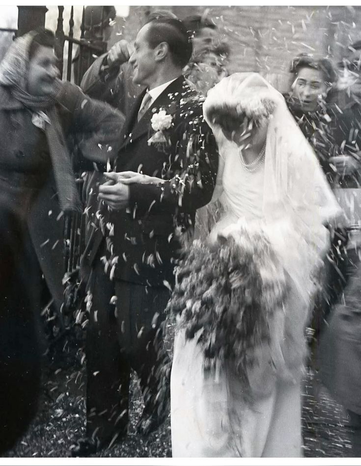 Vintage black and white wedding photo of bride and groom being showered with confetti by guests outside a church.