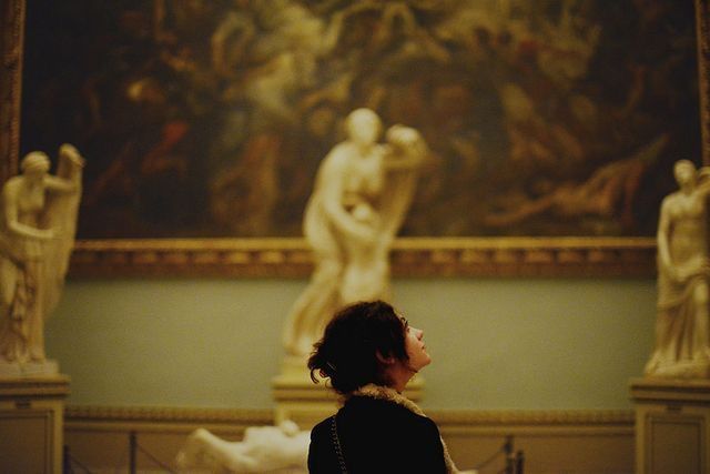 Person admiring classical sculptures and a large Renaissance painting in an elegant museum gallery.