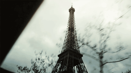 Low-angle view of the Eiffel Tower in Paris against a cloudy sky, framed by bare winter trees.