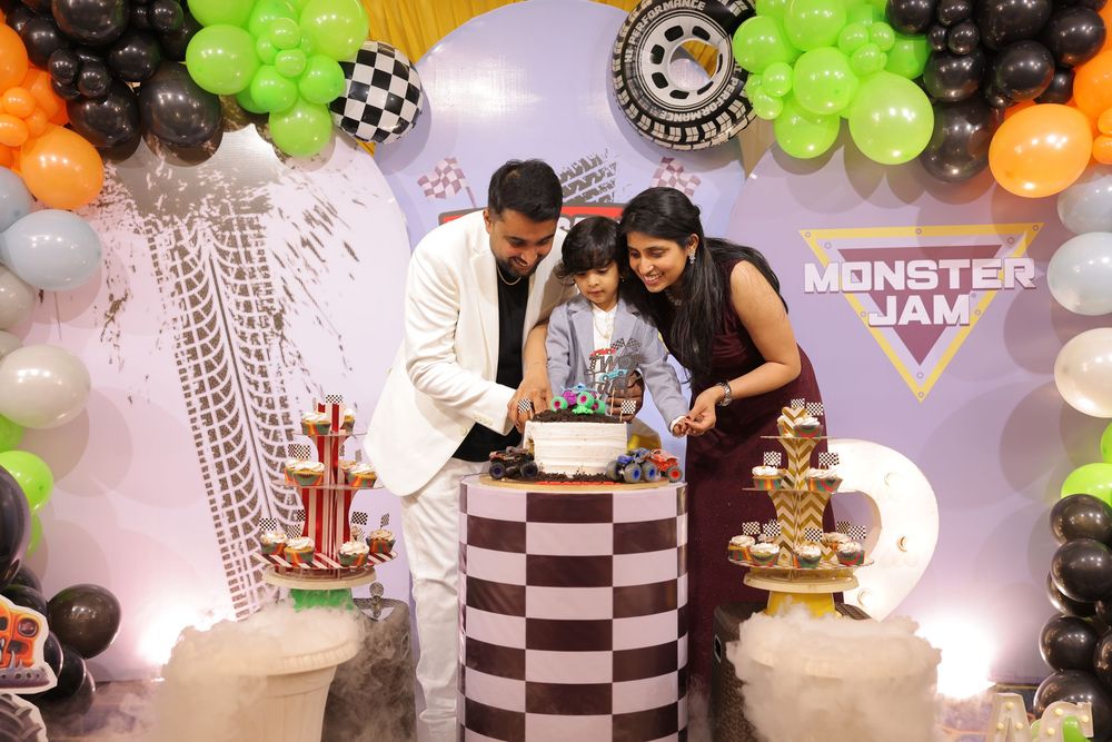 Family cutting cake at a Monster Jam themed birthday party with colorful balloon decorations.