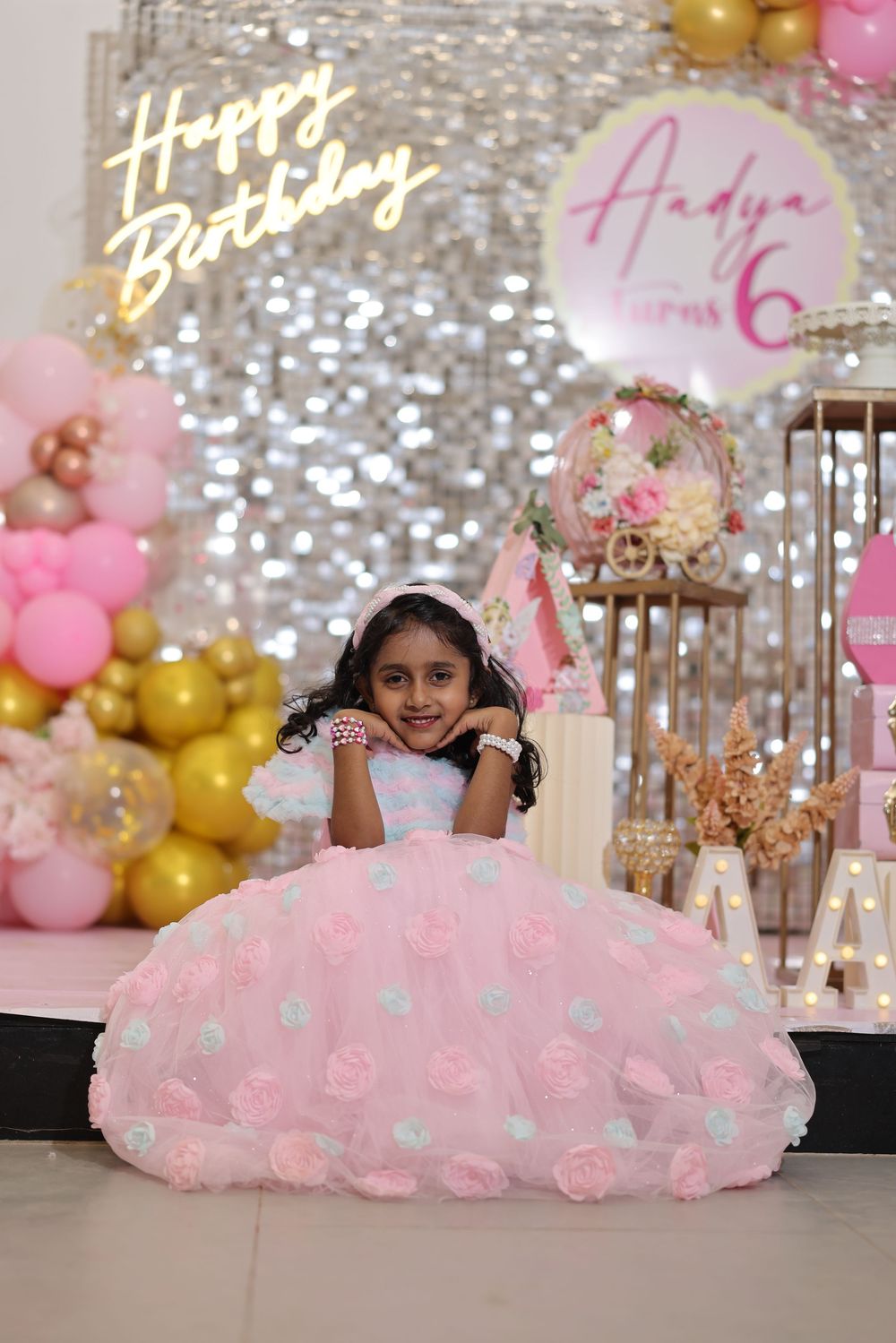 A young girl in a pink floral ball gown poses at her 6th birthday party with balloon decor.