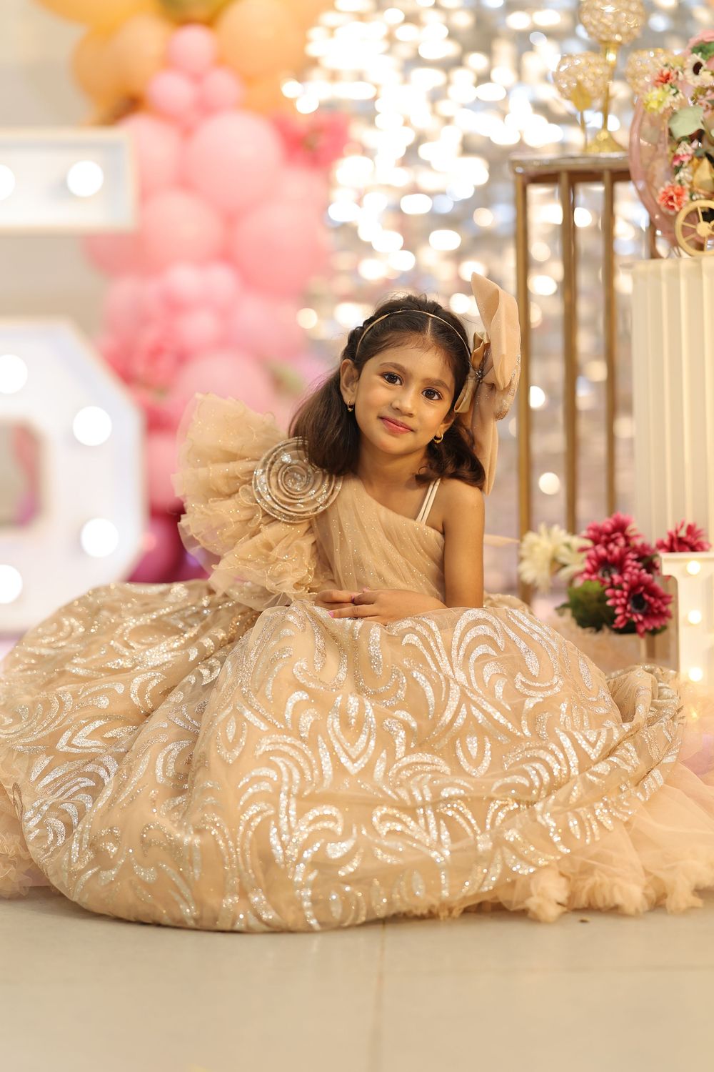 Young girl in gold sequin ball gown poses at a festive birthday party with balloon decorations.