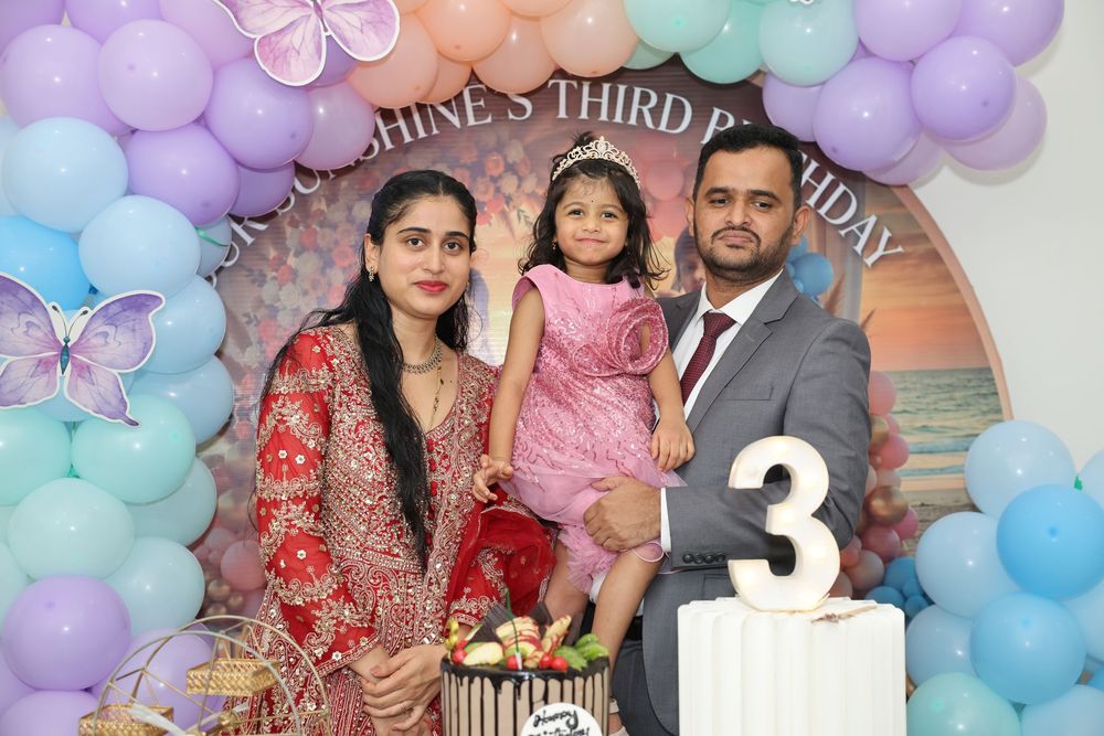 Family posing at a little girl's third birthday party with balloon arch, butterfly decorations, and number 3 sign.