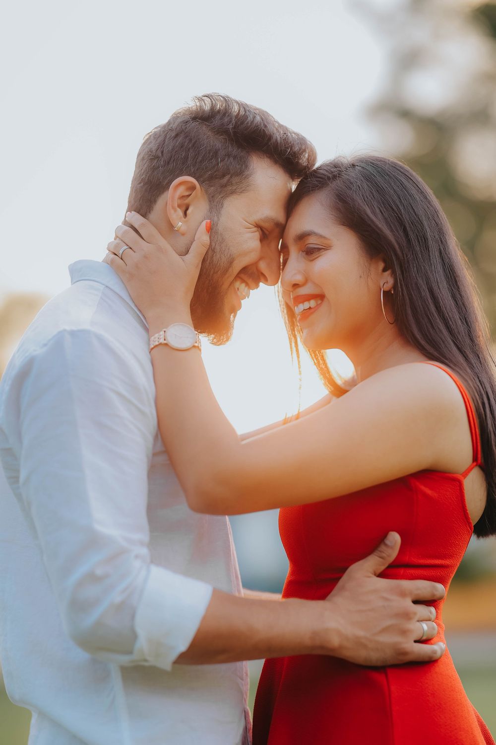 Couple in golden sunset light, foreheads touching, smiling in a tender romantic embrace.