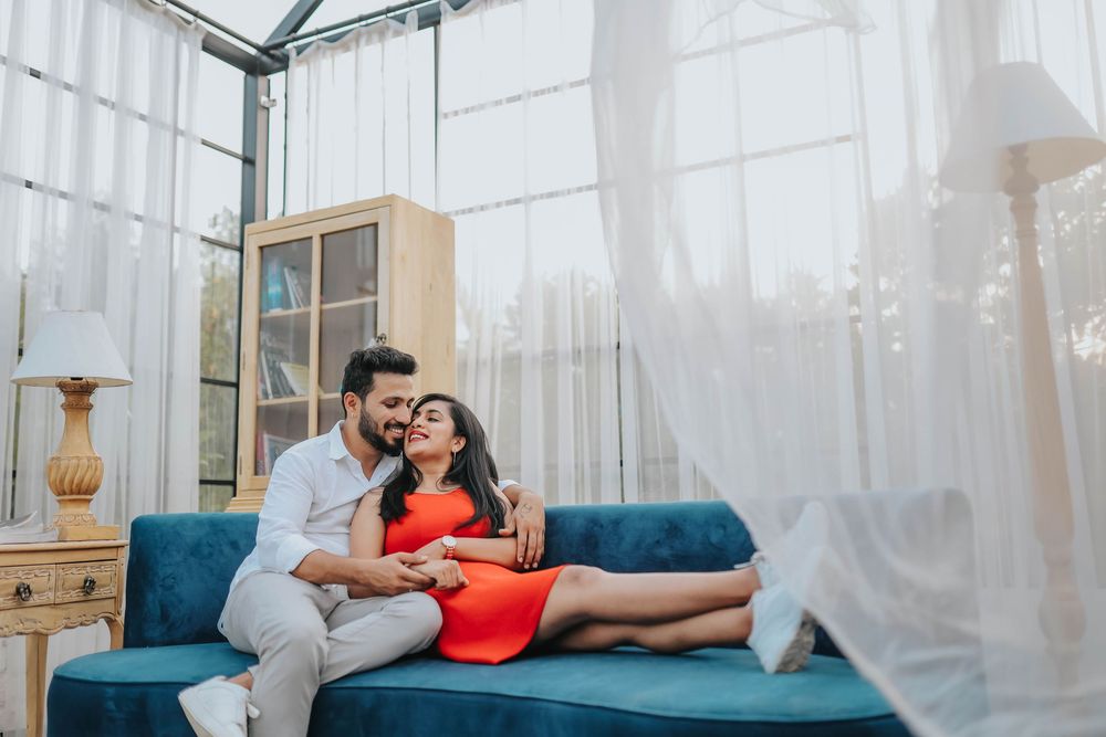 Romantic couple cuddling on a blue sofa in a bright, elegant room with sheer curtains.