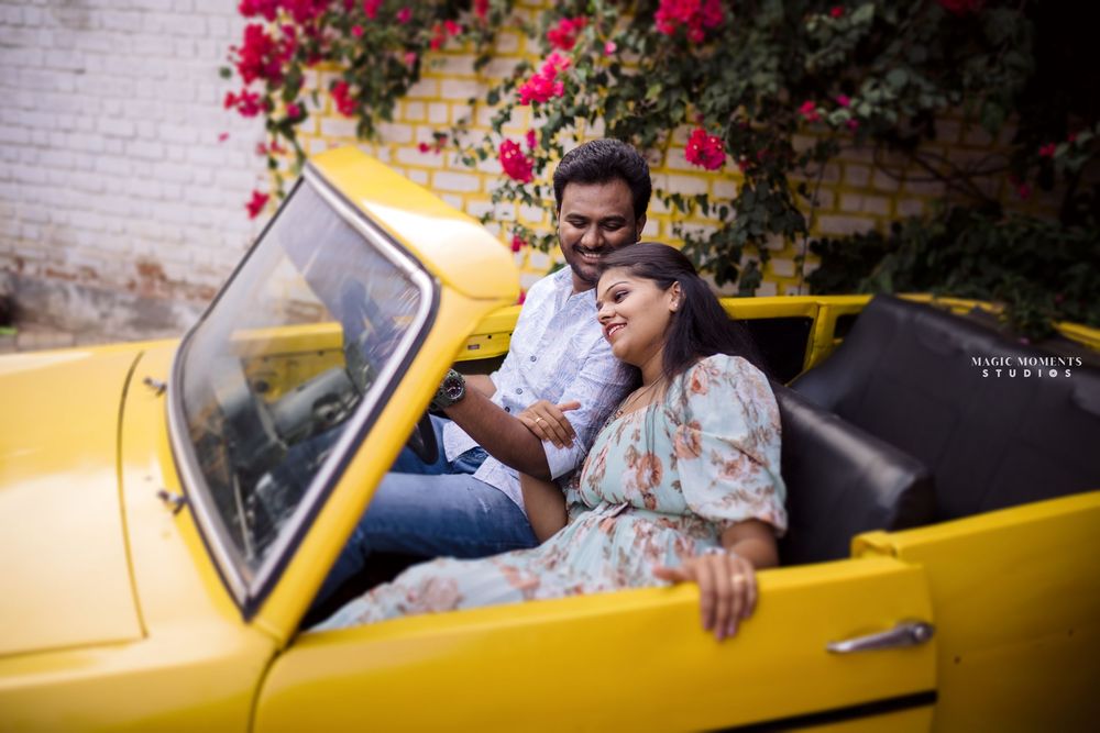 Happy couple sitting in a vintage yellow convertible car surrounded by blooming flowers.