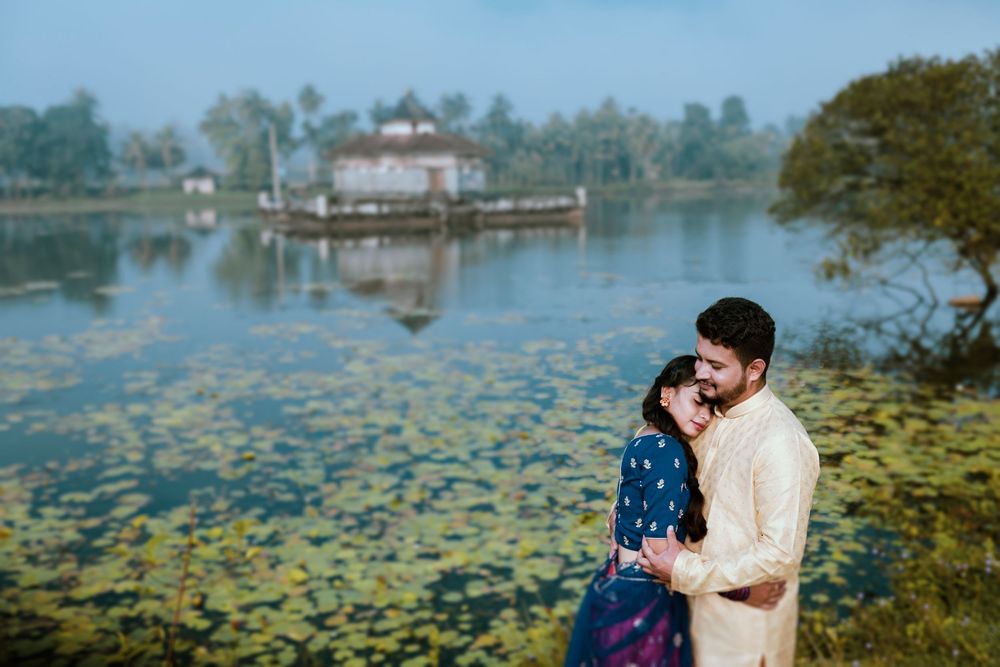 Romantic couple embracing near a serene lake with lily pads and a misty temple in the background.