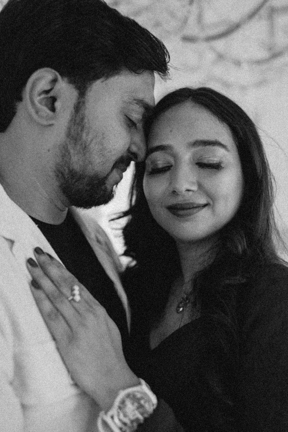 Black and white romantic couple portrait with foreheads touching, woman wearing engagement ring and necklace.