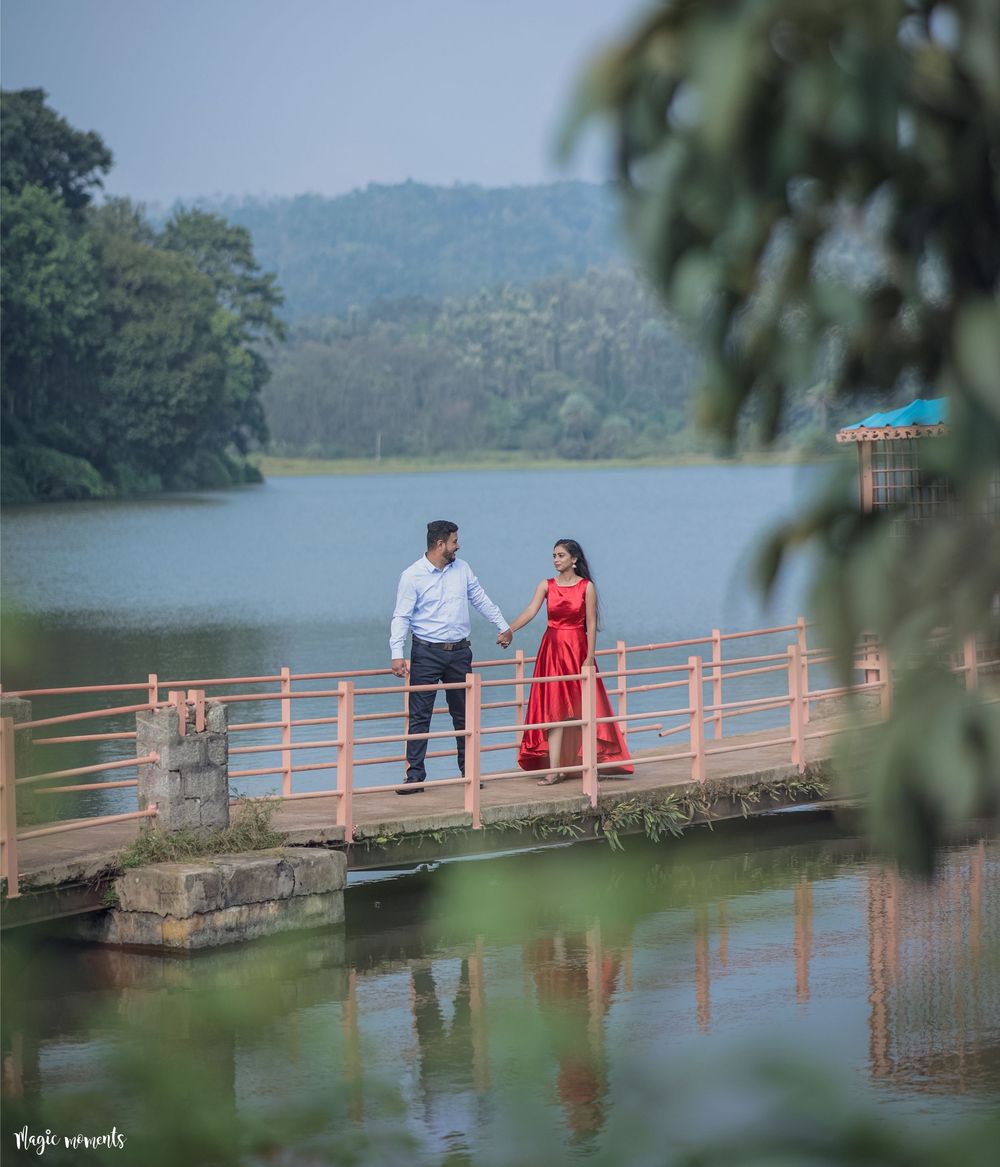 Couple holding hands on a bridge over a serene lake, woman in a flowing red dress.
