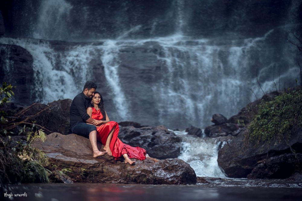 Couple sitting on rocks in front of a dramatic waterfall, woman in flowing red dress.