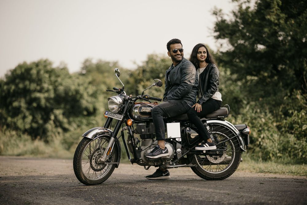 Stylish couple in black leather jackets posing on a classic motorcycle on an open road.