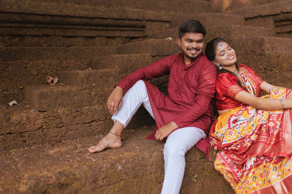 Indian couple in traditional attire sitting on stone steps, smiling and leaning on each other.