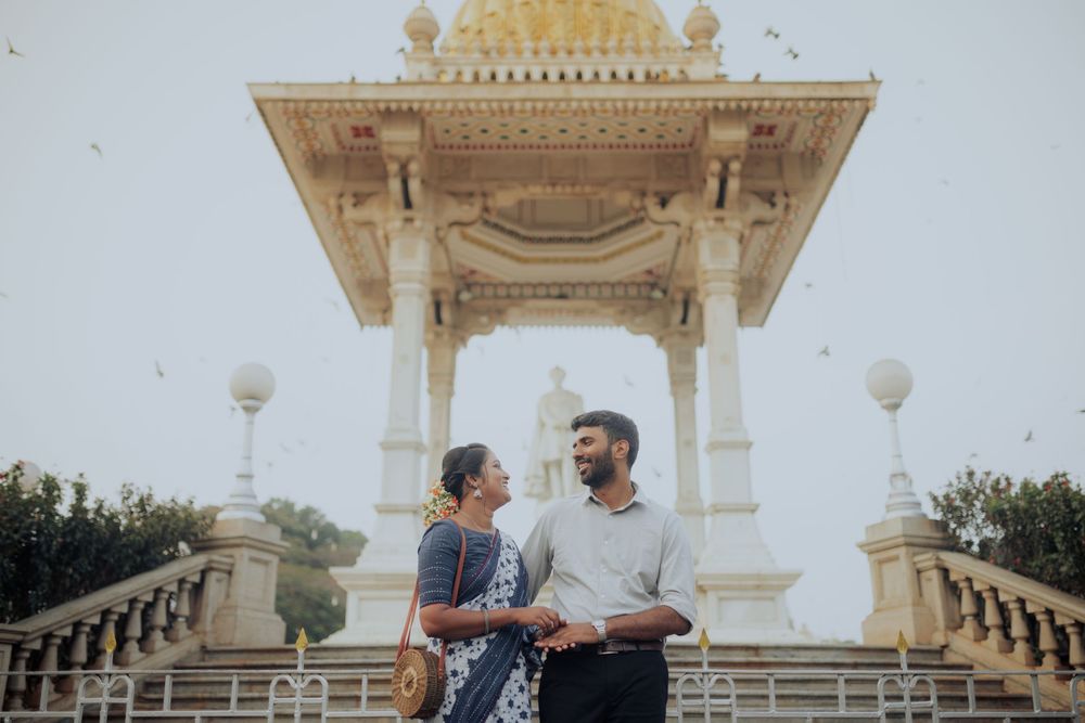 Couple standing together in front of an ornate temple gazebo structure under a clear sky.