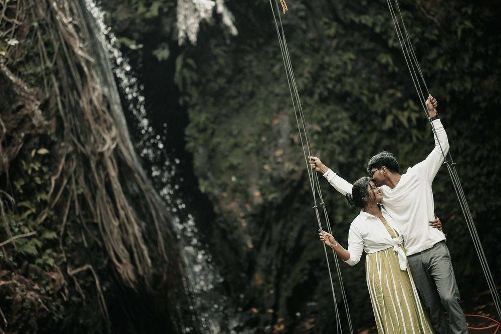 Couple holding ropes near a lush waterfall, sharing a romantic moment in nature.