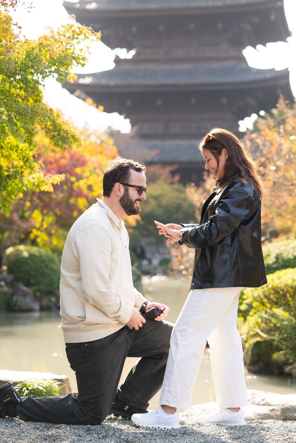 Man proposing on one knee to woman at Japanese temple with autumn foliage and pagoda backdrop.