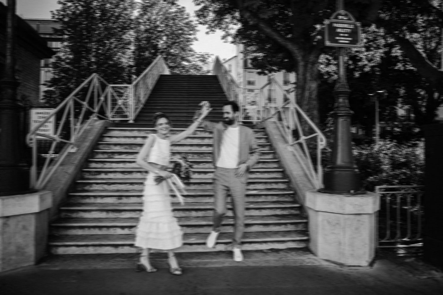 Black and white photo of a joyful couple jumping on stone steps in Paris, France.