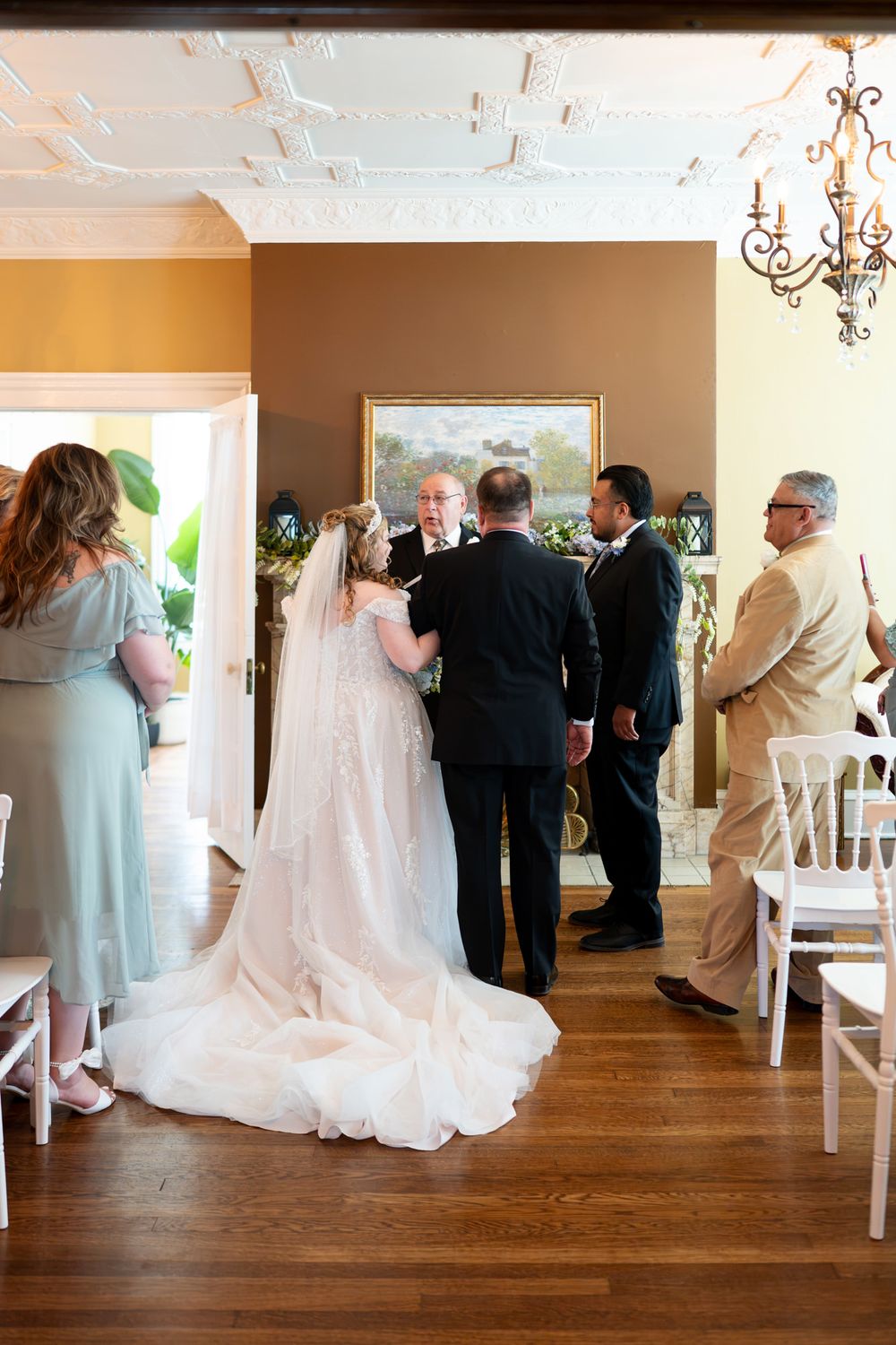 Elegant indoor wedding ceremony with bride in flowing gown and veil, surrounded by guests in a decorated venue.