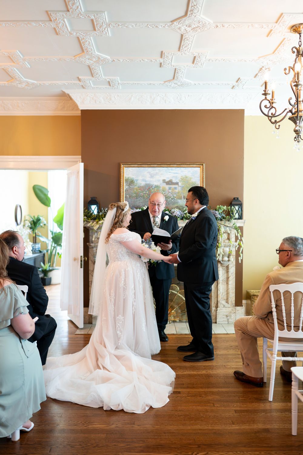 Bride and groom exchange vows during intimate indoor wedding ceremony with ornate ceiling.